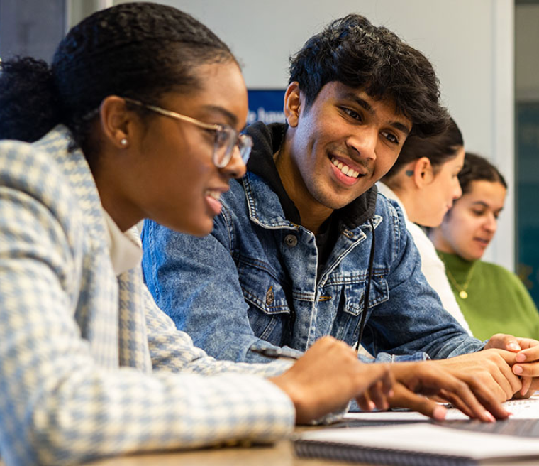 Closeup view of students sitting side by side looking at content on a laptop just out of frame in a shared study space